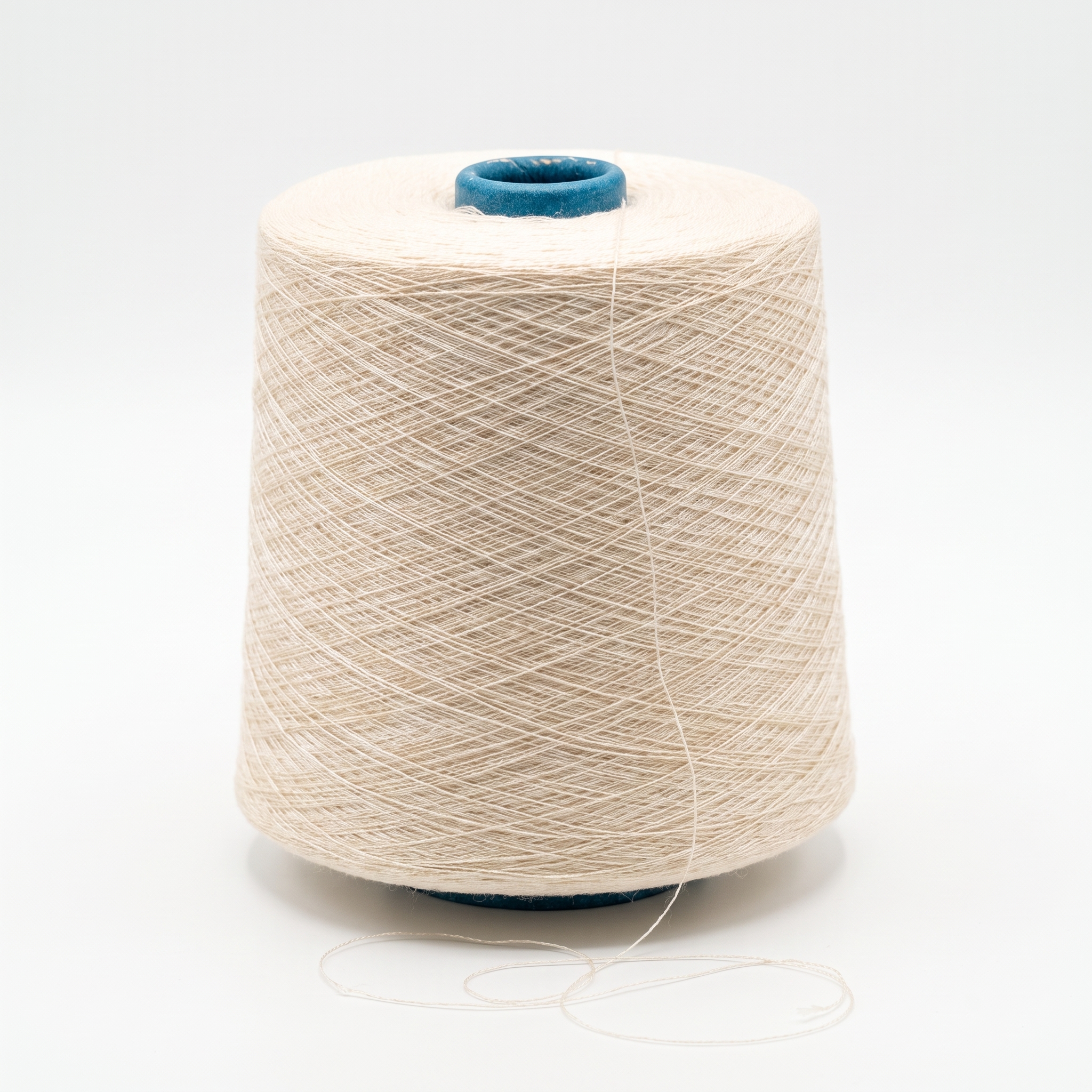 En stor cone med beige garn står på en vit yta, och en lös tråd ligger framför.