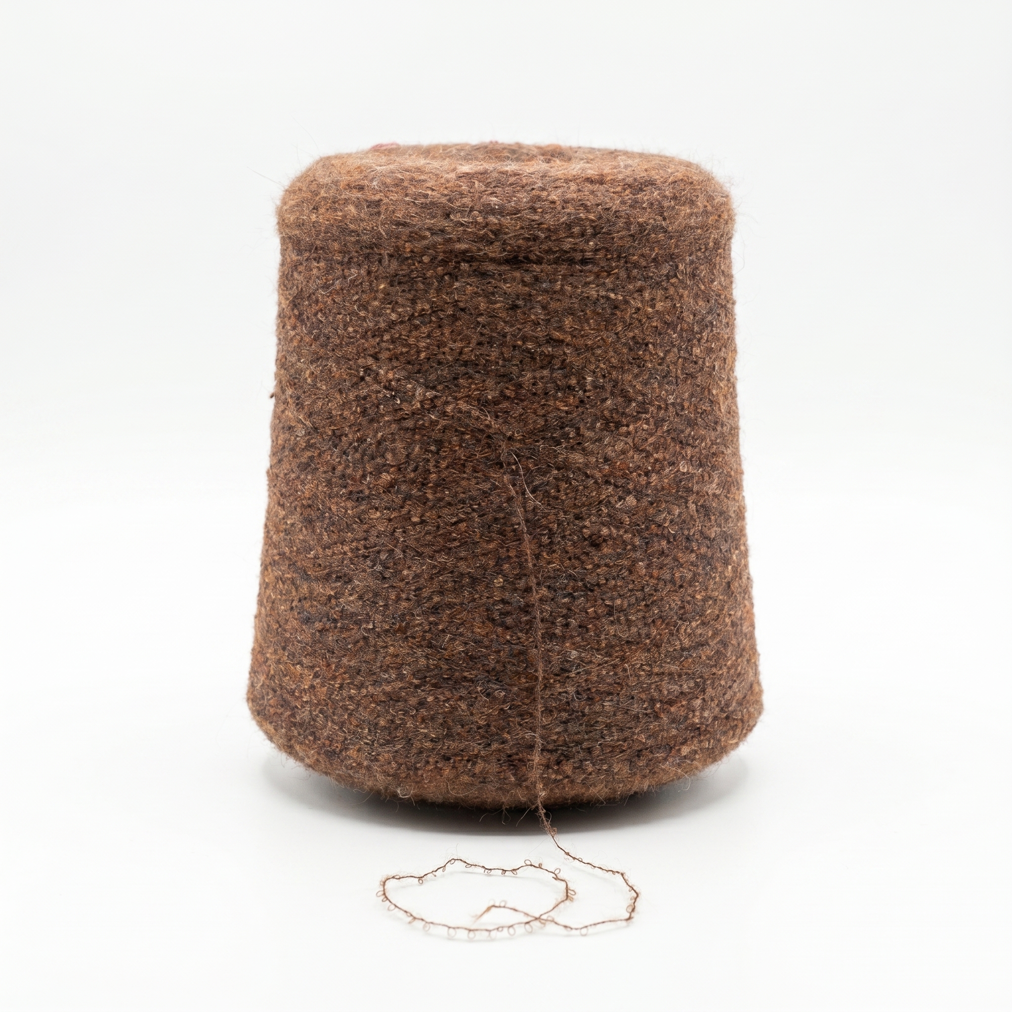 En stor cone med mörkbrunt, texturerat garn med en lös tråd framför på en vit bakgrund.