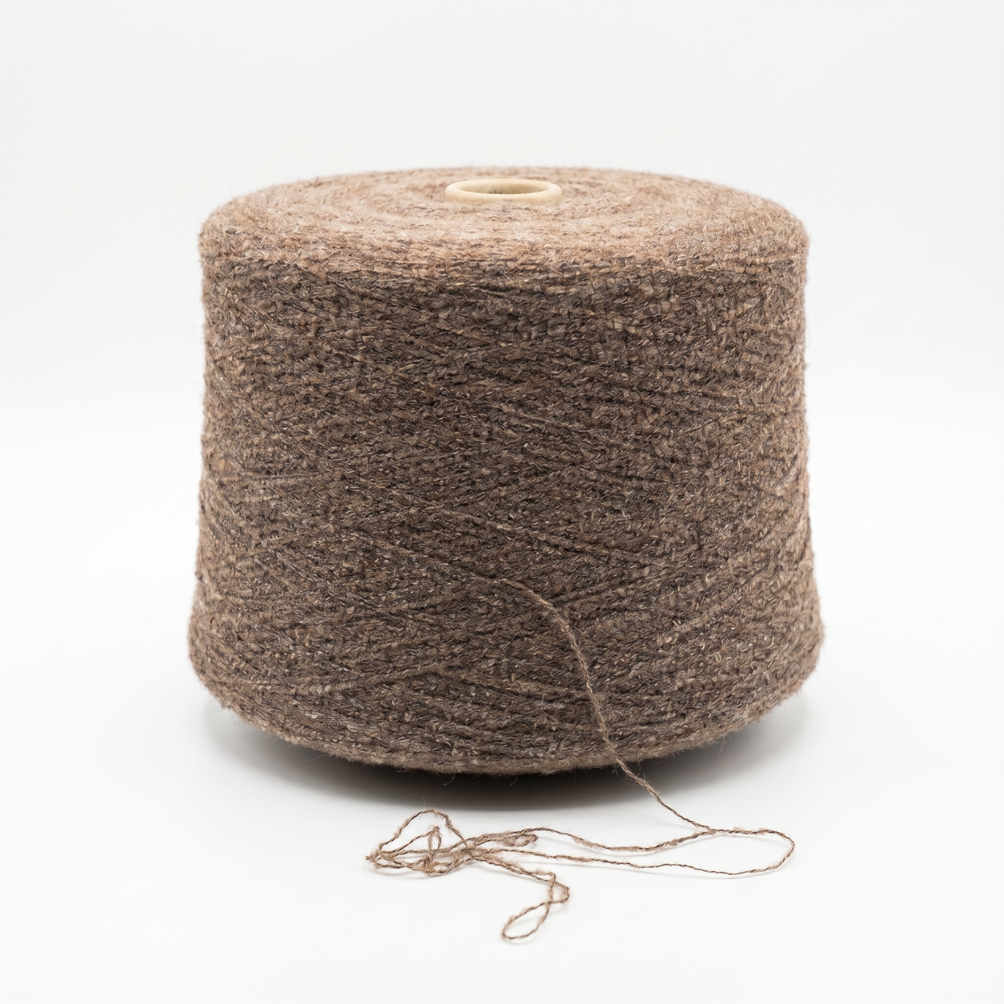En cone med brunt, texturerat garn och en lös tråd som ligger framför på den vita ytan.