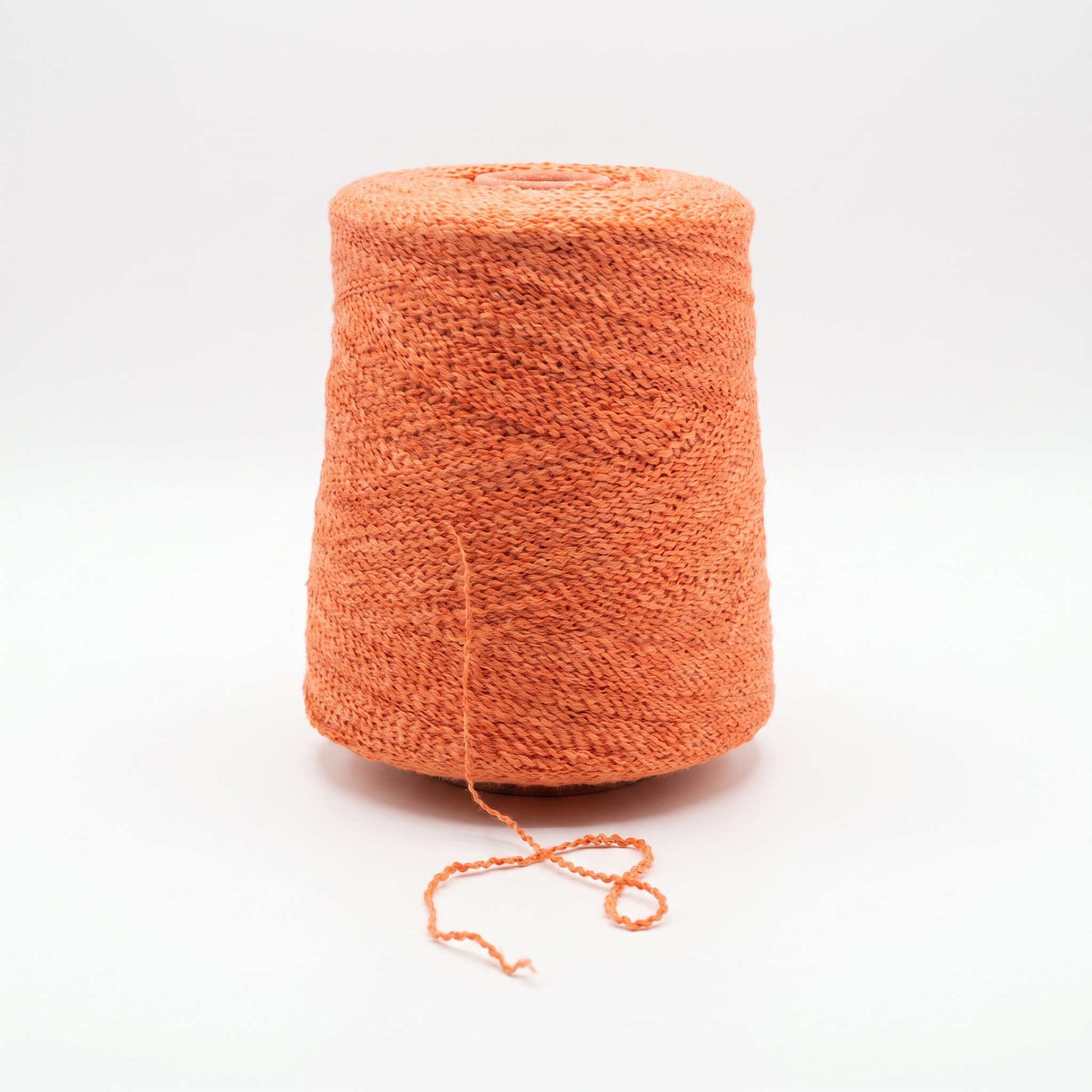 En cone med orange, texturerat garn på en vit bakgrund.