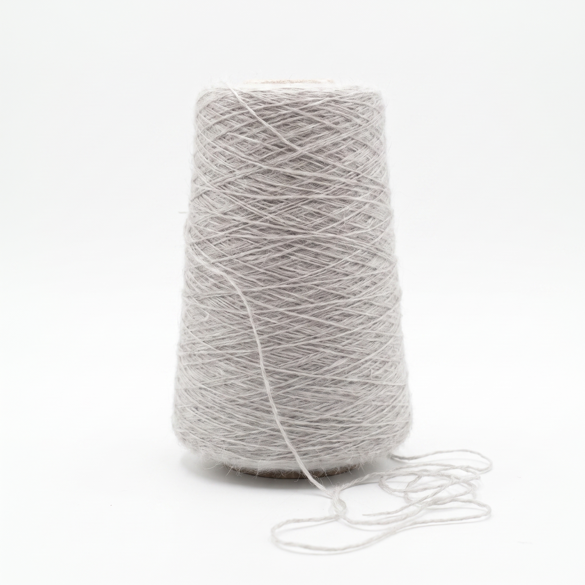 En cone med ljusgrått, fiberrikt garn och en lös tråd framför på en vit bakgrund.